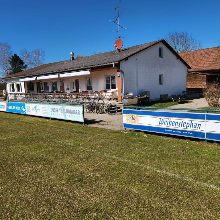 Biergarten und Sportgaststätte zum Kiesweiher Großes Sportgelände mit einem Vereinsgebäude und einer Terrasse, umgeben von Wiese.